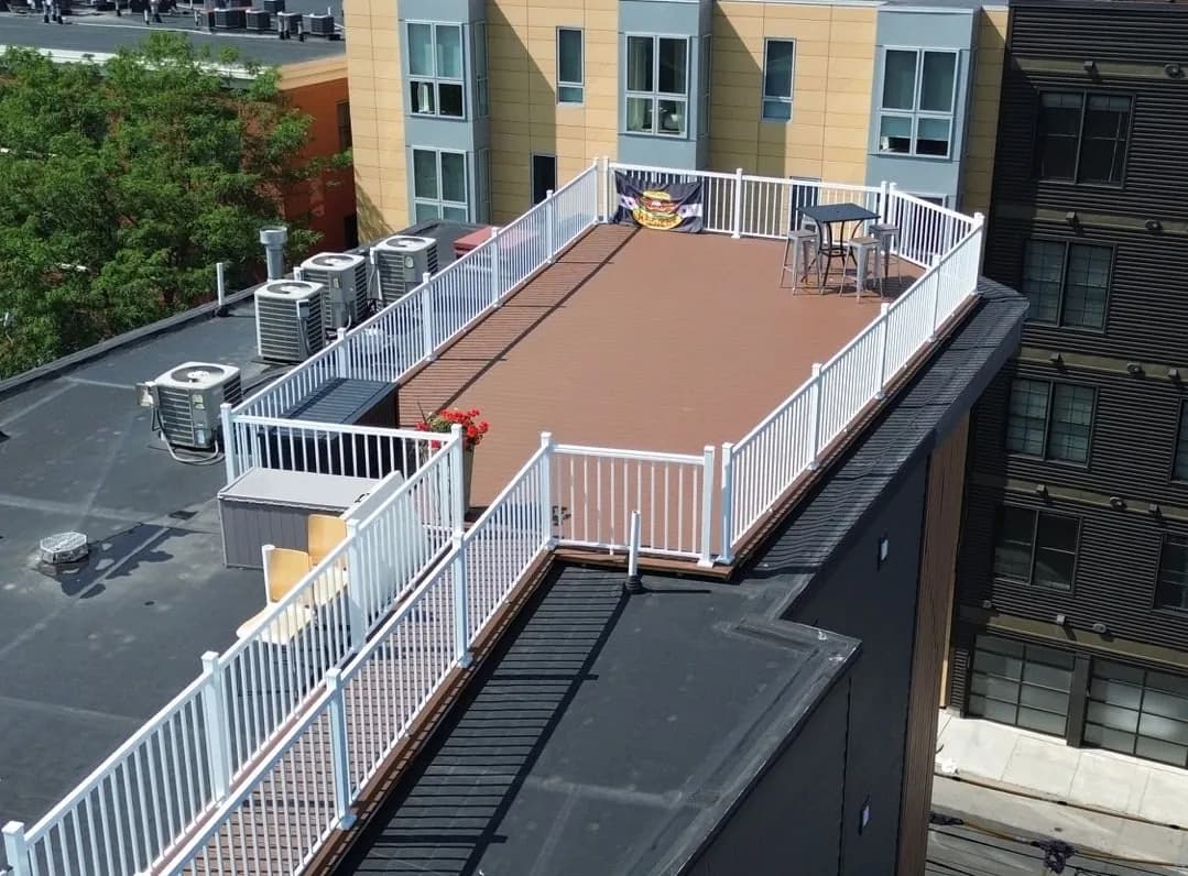 Rooftop deck with brown composite decking and a white railing around its edge, on top of a multi-story building
