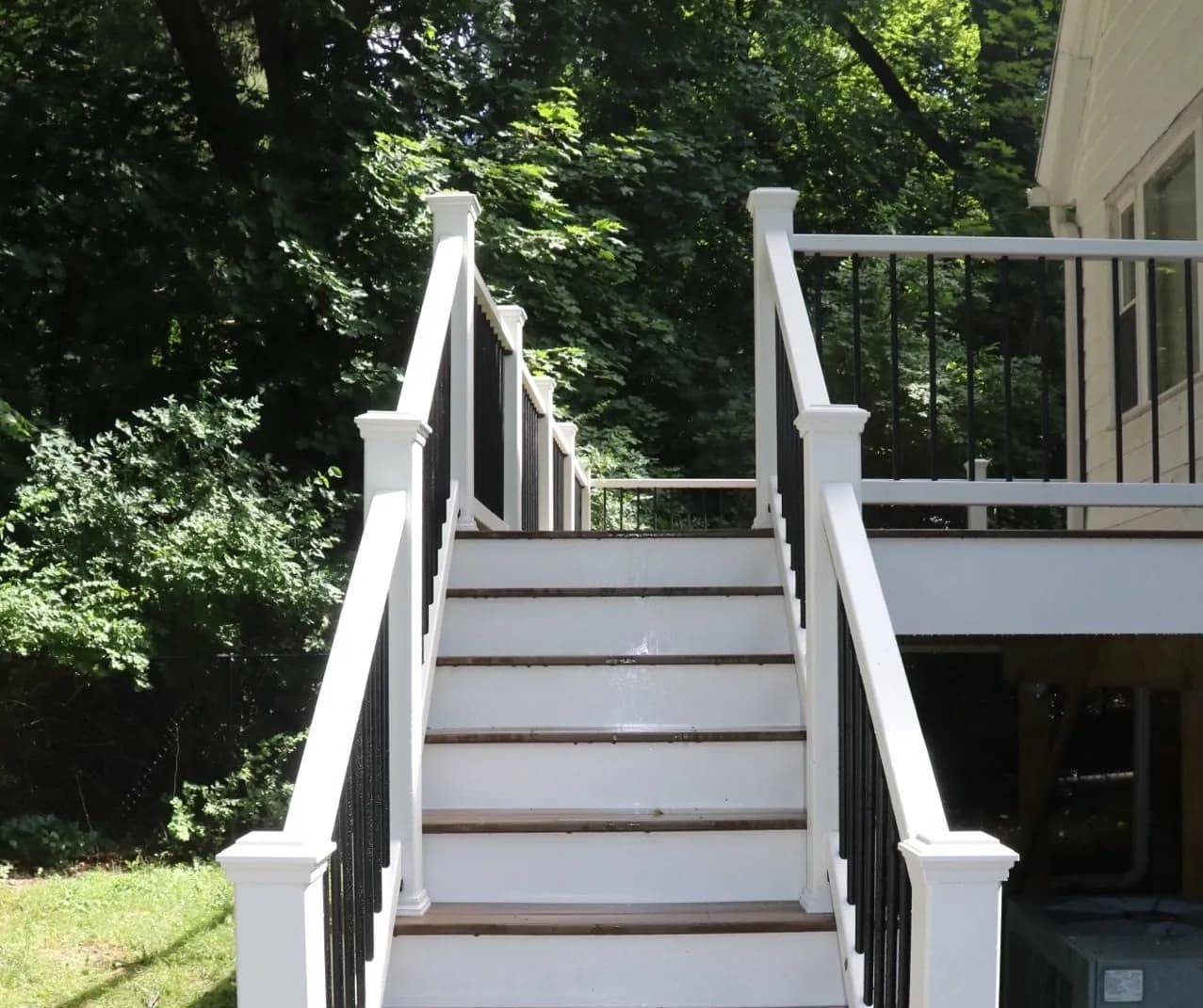 Composite deck stair run with white risers, brown treads, white posts, and black balusters leading up to a raised deck