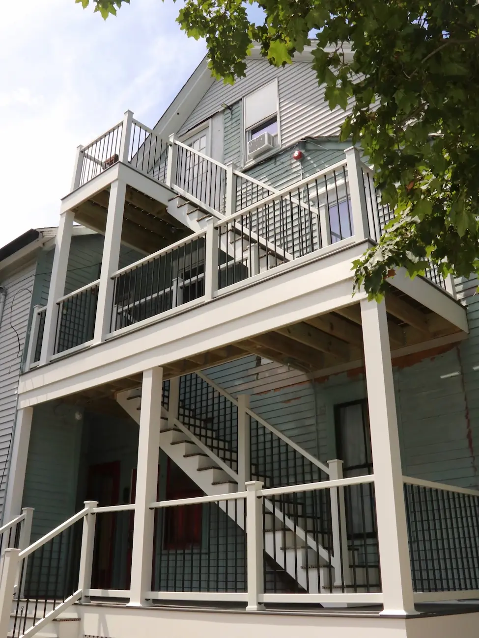 Three stacked deck levels on a gray three-story house, with white PVC posts and rail, black balusters and stairs linking each level