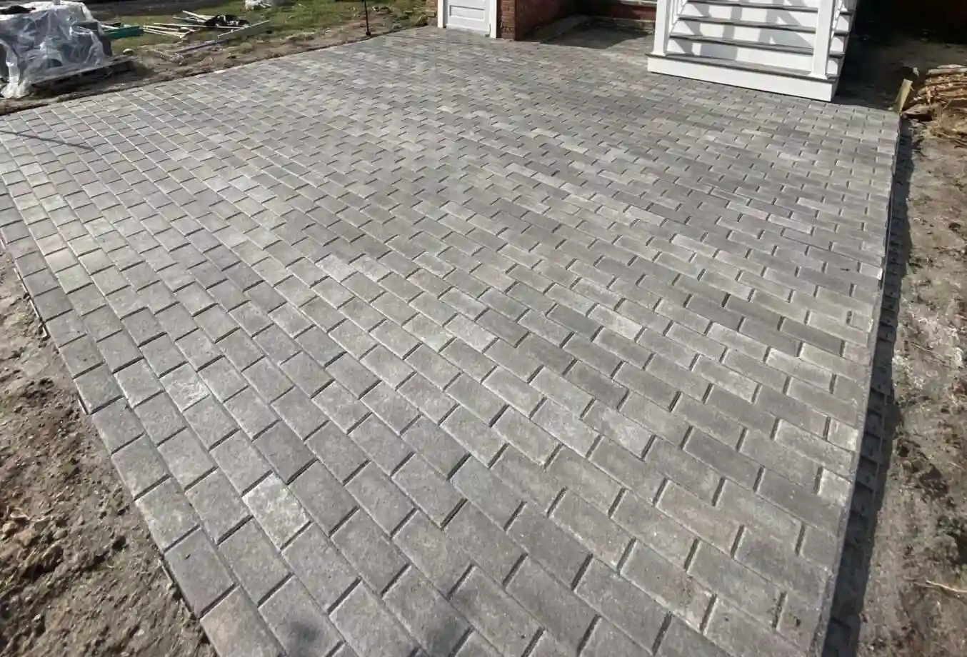 Concrete paver patio laid in a herringbone pattern with a soldier-course border, photographed mid-install before the surrounding grade was finished