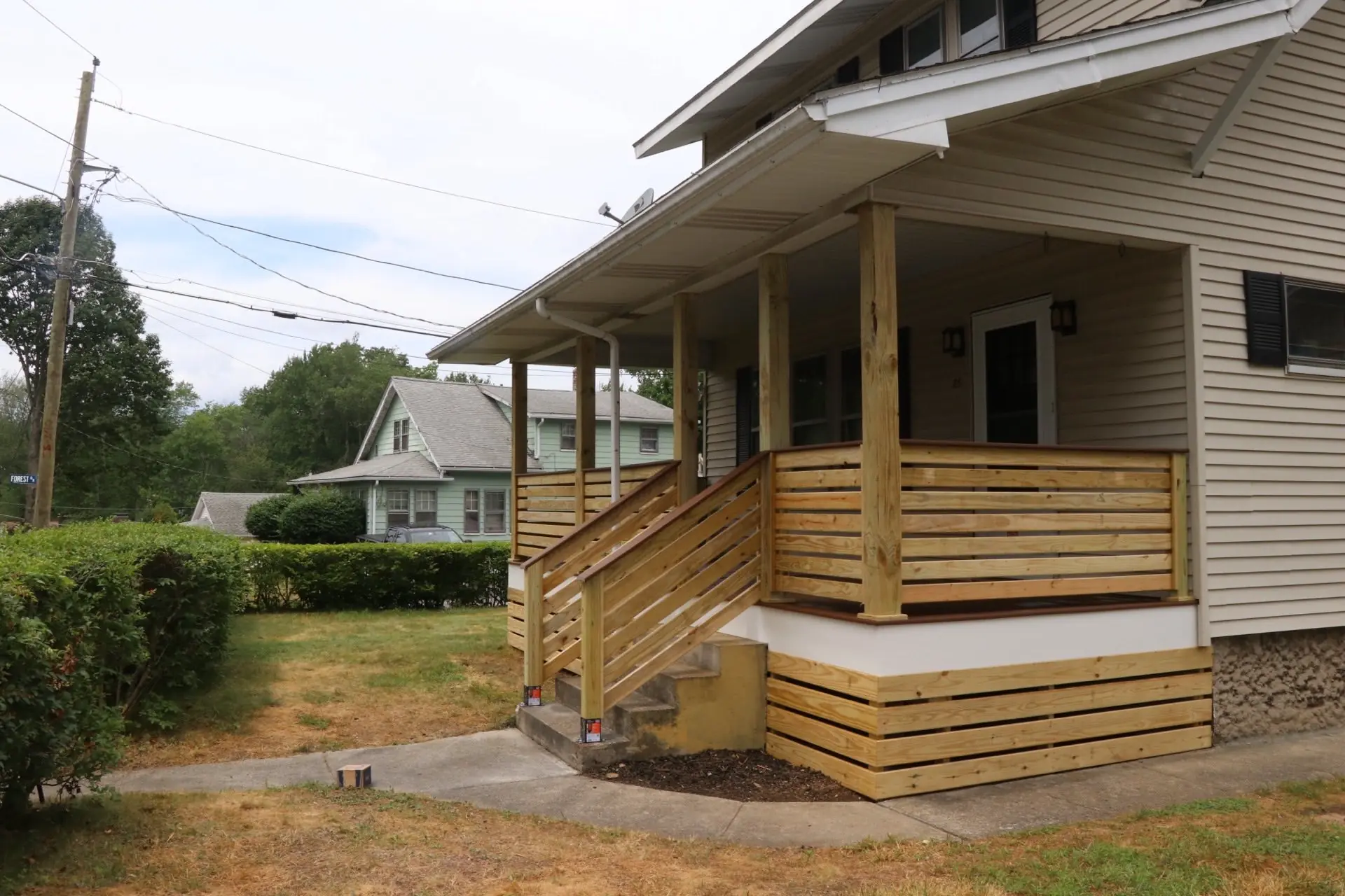 Covered farmers porch with a horizontal-slat pressure-treated railing and matching skirt, with steps down to a concrete walk