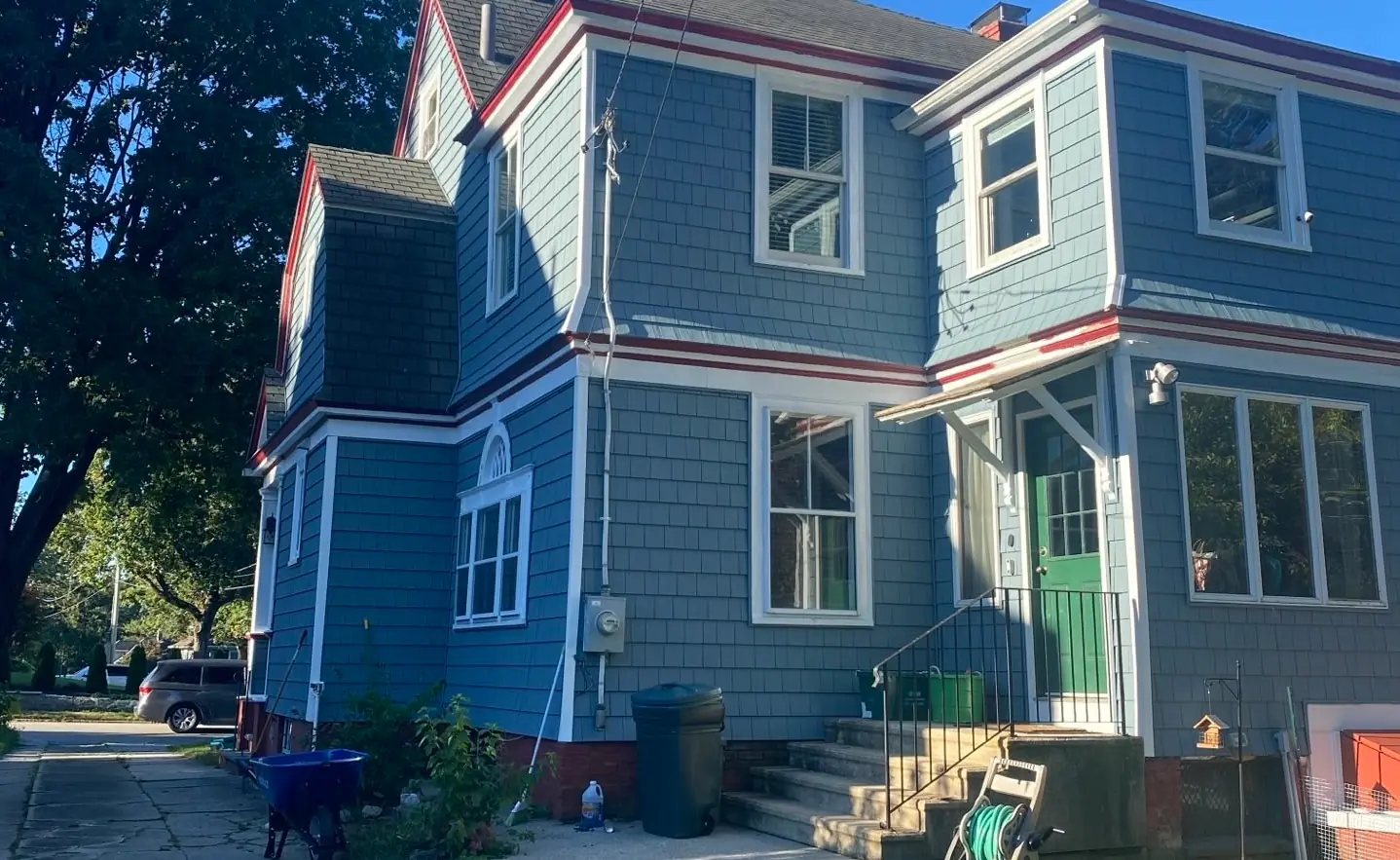Two-story house in blue shingle siding with red trim and a green front door under a small entry roof